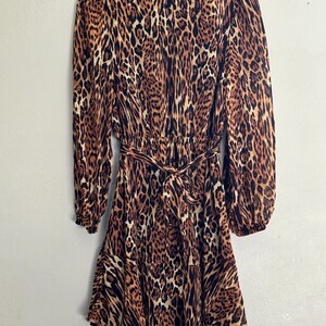 Puede incluir: Un vestido de estampado de leopardo marr&oacute;n y negro con mangas largas y un lazo en la cintura.