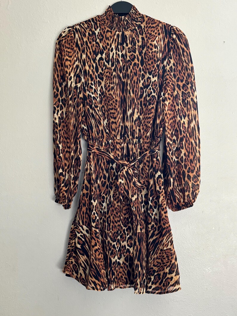 Puede incluir: Un vestido de estampado de leopardo marr&oacute;n y negro con mangas largas y un lazo en la cintura.
