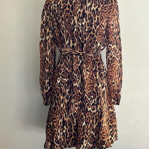 Puede incluir: Un vestido de estampado de leopardo marr&oacute;n y negro con mangas largas y cintura con lazo. El vestido tiene cuello alto y un dobladillo con volantes.