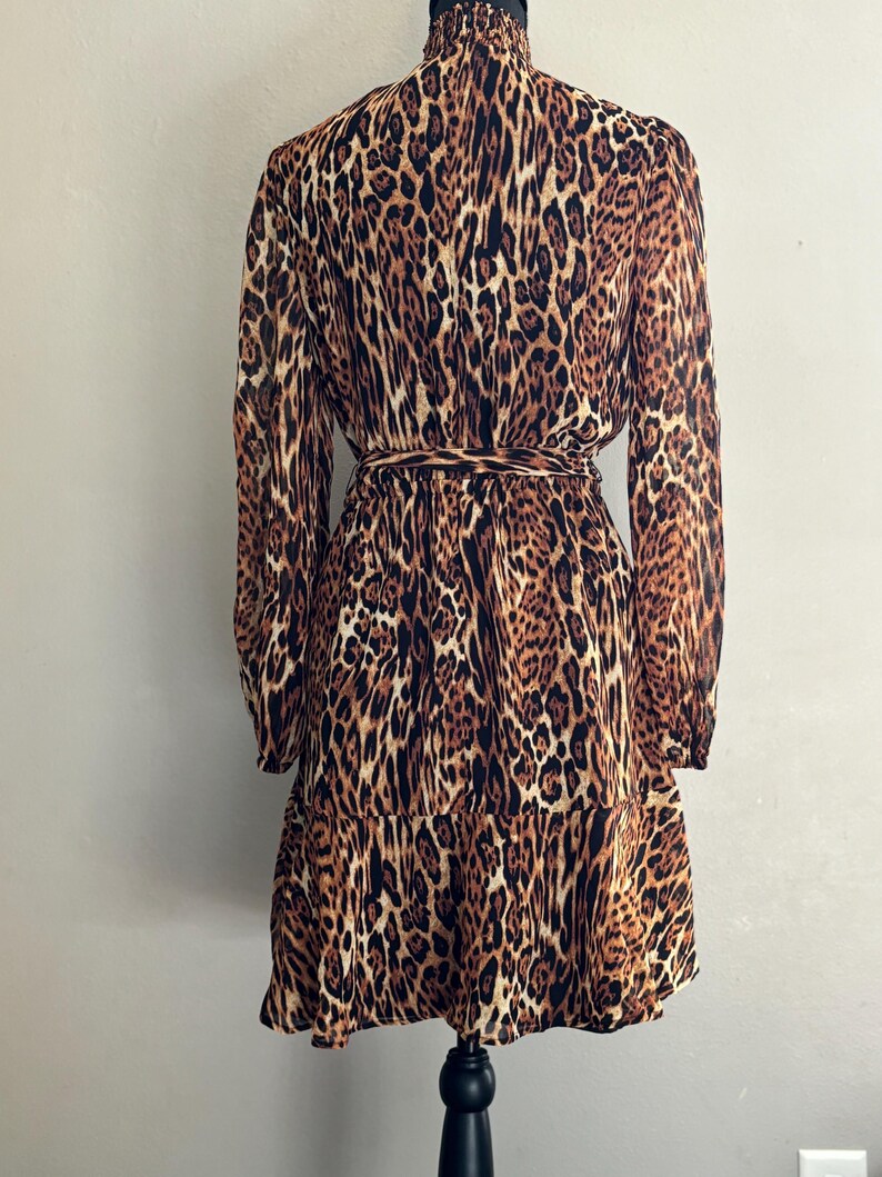 Puede incluir: Un vestido de estampado de leopardo marr&oacute;n y negro con mangas largas y cintura con lazo. El vestido tiene cuello alto y un dobladillo con volantes.