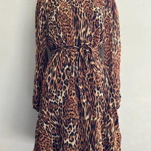 Puede incluir: Un vestido de estampado de leopardo marr&oacute;n y negro con cuello alto, mangas largas y cintur&oacute;n de lazo. El vestido tiene una falda de capas.