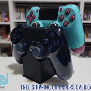 Peut inclure: Deux manettes de jeu PlayStation 4, l'une noire et l'autre turquoise, sont empilées sur un support noir. La manette du haut est turquoise avec des accents marrons et la manette du bas est noire avec des accents bleus. Les manettes sont sur une surface blanche.