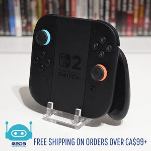 May include: Black Nintendo Switch controller with blue and orange joysticks. The controller has buttons labeled X, Y, A, and B. The text "Nintendo Switch" is visible on the controller. The controller is displayed on a clear stand.