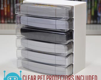 May include: A white plastic storage case with six clear plastic slots for storing video game cartridges. The case is designed to hold Super Nintendo Entertainment System (SNES) cartridges. The text "CLEAR PET PROTECTORS INCLUDED" and "FREE SHIPPING ON ORDERS OVER CA$99+" is printed on the bottom of the image.