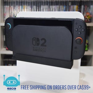 May include: A black Nintendo Switch console with attached controllers, resting on a white stand. The console has blue and orange accents on the controllers. The text "002 Nintendo Switch" is visible on the console.