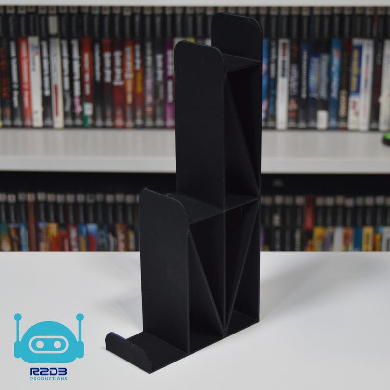 May include: A black plastic stand with multiple compartments for organizing video game cartridges. The stand is designed to hold multiple cartridges vertically.
