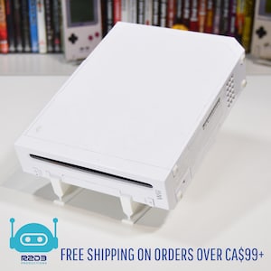 May include: A white Nintendo Wii console, rectangular with a disc slot and the word "Wii" on the front. It's raised on white supports. The image also includes the text "R2D3 Productions". The console is a popular home video game console.