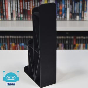 May include: Black plastic video game storage stand with multiple compartments. The stand is designed to hold video game cartridges and is labeled "R2D3 Productions".