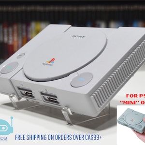 May include: A white PlayStation 1 console with a clear acrylic stand. The console has a gray disc drive and a PlayStation logo on the top. The text "FOR PS1 "MINI" ONLY" is visible in the lower right corner of the image.