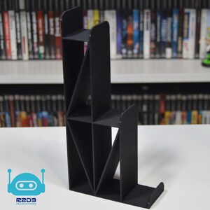 May include: Black, geometric, tiered stand for displaying video games. The stand has multiple shelves and is made of a sturdy material.