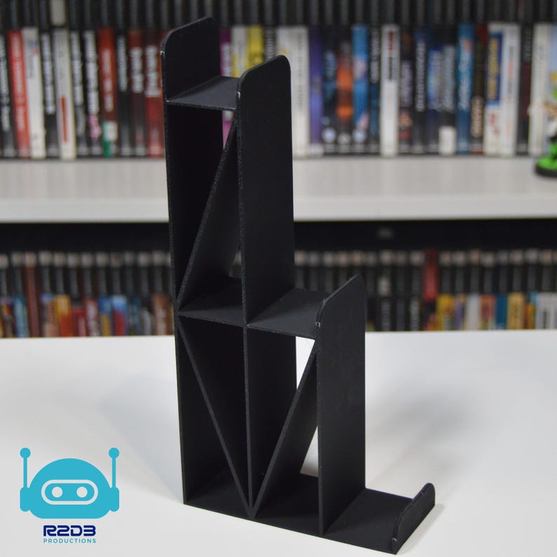 May include: Black, geometric, tiered stand for displaying video games. The stand has multiple shelves and is made of a sturdy material.