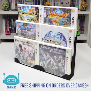 Könnte beinhalten: Ein schwarzer, mehrstufiger Displayständer mit sechs Nintendo 3DS-Spielhüllen. Die Spielhüllen zeigen farbenfrohe Kunstwerke und Titel wie "Dragon Quest", "Fire Emblem Fates" und "Final Fantasy". Der Ständer steht auf einer weißen Oberfläche.
