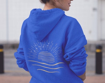 Puede incluir: Una sudadera con capucha azul real con un gráfico blanco de una salida del sol sobre el océano con pájaros volando por encima.