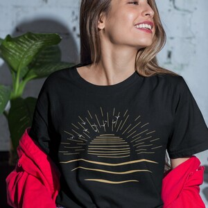 Może przedstawiać: Czarny T-shirt z złotym nadrukiem wschodu słońca nad oceanem z ptakami latającymi nad nim.