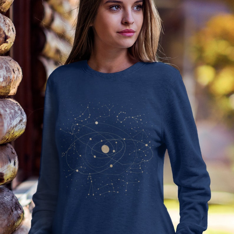 Puede incluir: Una sudadera azul marino con un dise&ntilde;o de constelaci&oacute;n que representa un sistema solar con planetas y estrellas. El dise&ntilde;o es de color dorado claro.