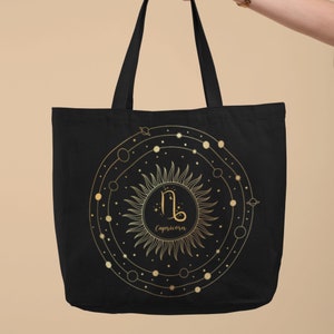 May include: Black canvas tote bag with a gold zodiac symbol for Capricorn, surrounded by a circle of stars and planets.