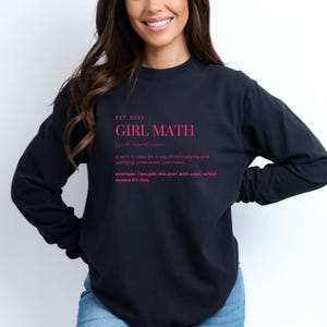 Può includere: Felpa nera a maniche lunghe con il testo "EST. 2023 GIRL MATH [guhl-maeth] noun a term to describe a way of rationalizing and justifying unnecessary purchases. example: I bought this shirt with cash, which means it's free." stampato in rosa.