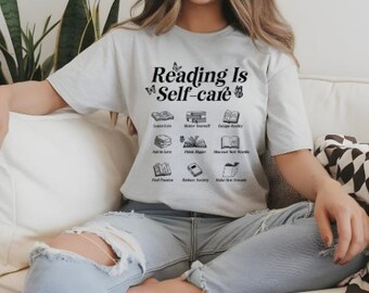May include: A white t-shirt with the text "Reading is Self-care" and a graphic of books with butterflies. The text is in black and the books are in grey.
