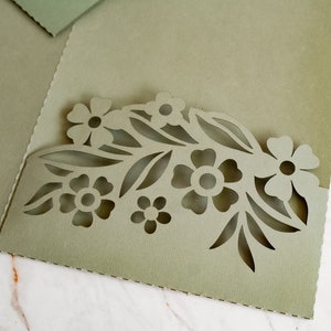 May include: A green cardstock invitation with a cut-out design of flowers and leaves. The design is in the shape of a half-circle.