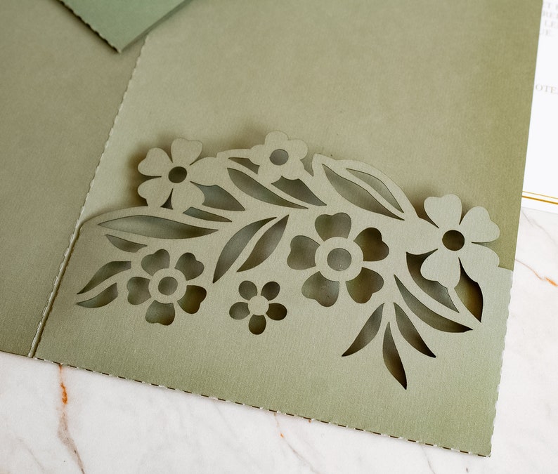 May include: A green cardstock invitation with a cut-out design of flowers and leaves. The design is in the shape of a half-circle.
