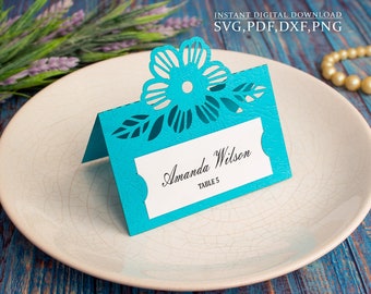 May include: A turquoise blue place card with a cut-out floral design. The card says "Amanda Wilson, Table 5".