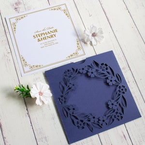 May include: A white card with gold lettering that says "Save the Date Stephanie & Henry" and a blue card with a cut-out floral design.