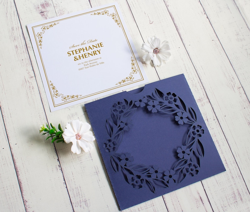May include: A white card with gold lettering that says "Save the Date Stephanie & Henry" and a blue card with a cut-out floral design.