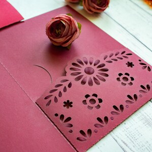 Puede incluir: Cartulina roja burdeos con un dise&ntilde;o decorativo de corte con flores y hojas. La cartulina est&aacute; doblada por la mitad para crear un bolsillo.