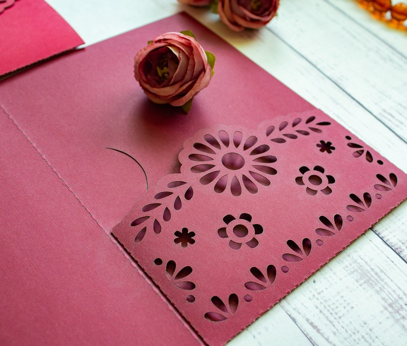 Puede incluir: Cartulina roja burdeos con un dise&ntilde;o decorativo de corte con flores y hojas. La cartulina est&aacute; doblada por la mitad para crear un bolsillo.