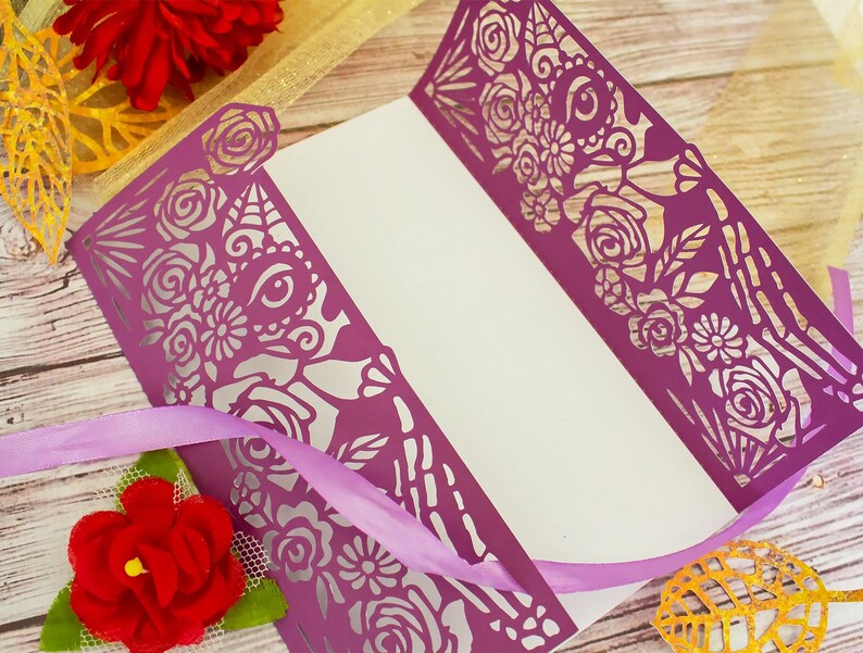 May include: Purple paper card with a cut-out design of flowers and a skull with an eye. The card is folded in half and has a white interior.