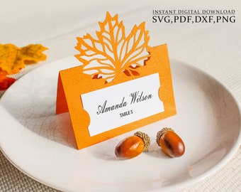 May include: An orange place card with a cut-out leaf design, featuring the name "Amanda Wilson" and "TABLE 5". Two acorns rest on a white plate. The words "INSTANT DIGITAL DOWNLOAD" and file types are visible.