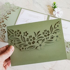 May include: A green folded card with a cut-out design of flowers and leaves. The card is folded in half and the front flap has a cut-out design of flowers and leaves. The card is blank inside.