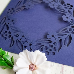 May include: A navy blue card with a floral design cut out around the edges. The card is blank inside and can be used for a variety of occasions.