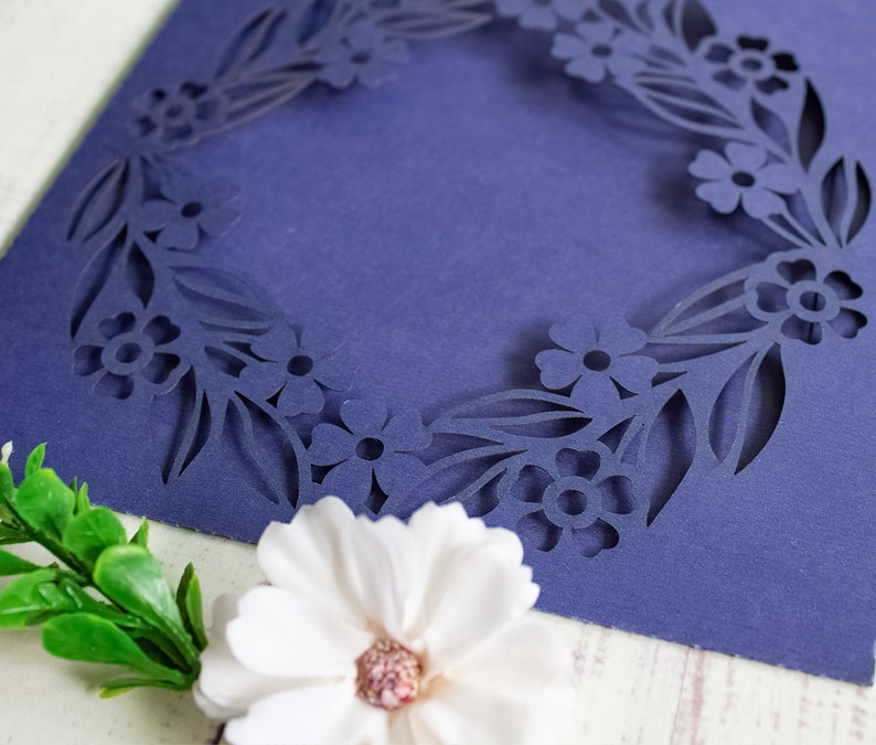 May include: A navy blue card with a floral design cut out around the edges. The card is blank inside and can be used for a variety of occasions.