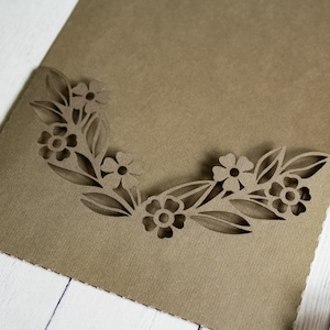 May include: A brown paper envelope with a decorative cut-out design of flowers and leaves around the edge.