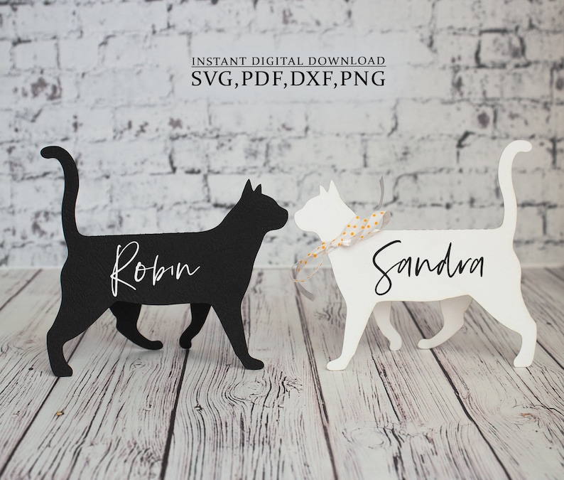 K&ouml;nnte beinhalten: Zwei schwarze und wei&szlig;e Katzen-Silhouetten-Platzkarte mit den Namen Robin und Sandra darauf. Die Platzkarte stehen auf einer Holzoberfl&auml;che.