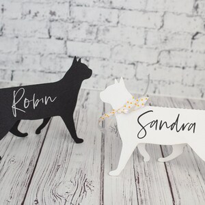 K&ouml;nnte beinhalten: Zwei schwarze und wei&szlig;e katzenf&ouml;rmige Platzkartehalter mit den Namen Robin und Sandra darauf geschrieben. Die Katze links ist schwarz und die Katze rechts ist wei&szlig;.