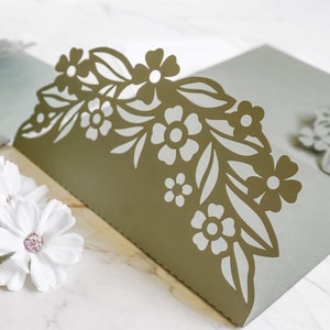 May include: A light green card with a decorative floral design cut out of the top edge. The design features leaves and flowers in a light gray color.