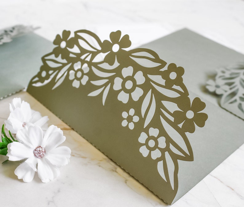May include: A light green card with a decorative floral design cut out of the top edge. The design features leaves and flowers in a light gray color.