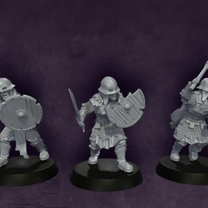 May include: Three grey plastic miniature figures of warriors wearing helmets and chainmail armour, holding swords and shields. The figures are standing on black circular bases.