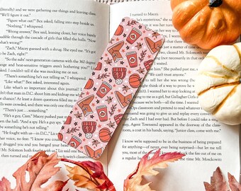 Könnte beinhalten: Ein rosa-oranges Lesezeichen mit Herbstthema. Das Lesezeichen zeigt verschiedene herbstliche Illustrationen, darunter Kürbisse, Kaffeetassen, Stiefel und Sterne. Das Lesezeichen ist mit einem rosa-orangenen Karomuster verziert. Das Lesezeichen ist eine großartige Möglichkeit, Ihren Platz in einem Buch zu markieren und Ihrem Leseerlebnis einen Hauch von Herbst zu verleihen.