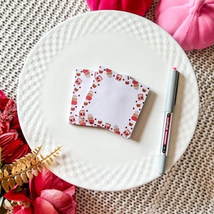 Peut inclure: Une assiette en céramique blanche avec une bordure décorative, présentant deux piles de notes autocollantes carrées avec une bordure sur le thème de l'automne composée de cupcakes et de pommes rouges et marrons. Un stylo argenté est également sur l'assiette.