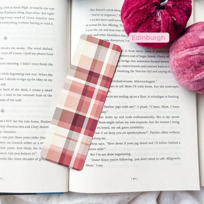 K&ouml;nnte beinhalten: Ein rechteckiger Lesezeichen mit einem Schottenmuster in Rot-, Rosa- und Beiget&ouml;nen liegt auf einem offenen Buch. Das Design des Lesezeichens ist ein Raster aus Quadraten. Das Wort "Edinburgh" ist auf einem rosa Etikett zu sehen.