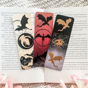 May include: Four bookmarks featuring dragons with different coloured backgrounds. The bookmarks are black, gold, red, and grey. The text on the bookmarks reads "Mysterious is on her heels and run to say that every time until we found Solomon's name, and in that order."
