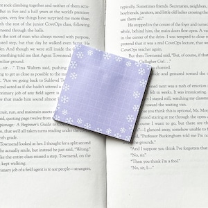 May include: A purple bookmark with a snowflake pattern. The bookmark is made of fabric and has a white border. The text "To recruit, run, and maintain assets" is visible on the page behind the bookmark.