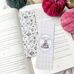 May include: Two decorative bookmarks lie on an open book. One has a pattern of books, coffee cups, and glasses. The other features a "Book Girl Fall Edition" design with a girl reading.