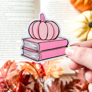 Peut inclure: Une citrouille rose est posée sur une pile de deux livres roses. Les livres sont fermés et on peut voir des pages blanches.