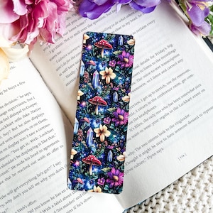 May include: A colourful bookmark with a galaxy background, featuring mushrooms, flowers, and crystals. The bookmark is designed with a whimsical and magical theme.