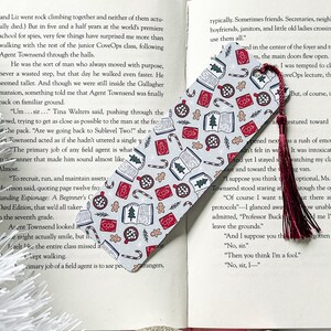 May include: A gray and white bookmark with a festive Christmas theme. The bookmark is covered in a repeating pattern of gingerbread cookies, candy canes, Christmas trees, and books. The bookmark has a red tassel.