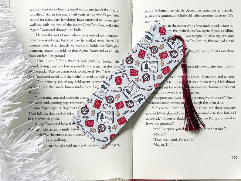 May include: A gray and white bookmark with a festive Christmas theme. The bookmark is covered in a repeating pattern of gingerbread cookies, candy canes, Christmas trees, and books. The bookmark has a red tassel.